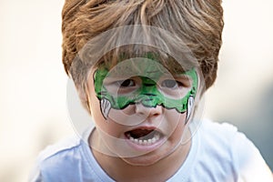 Dragon body art. Child with a mask on his face. Carnival. Favorite hero for a childrens party. Green face and fangs. A