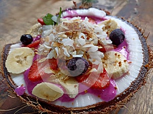 Dragon fruit smoothy in a natural traditional coconut fruit bowl on wooden table. Yogurt smoothie on coconut bowl.