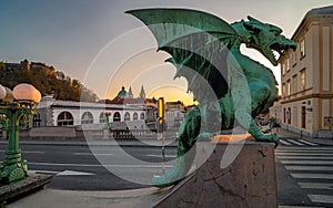 Dragon statue on Dragon bridge and Saint Nicholas Cathedral in background at sunset, Ljubljana, Slovenia