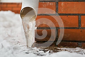 Drain pipe with frozen stream of water near house brick wall