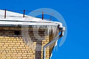 The drain pipe and icicles on the roof edge of the building