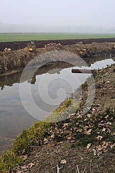 Drainage channel and a stream of water between fields on a foggy day in the italian countryside