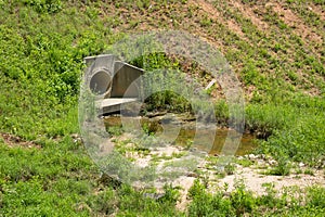 Drainage ditch lined with grass and weeds behind a subdivision