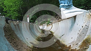 Drainage system in the forest. Water flowing through the channel. Two tourists stepping over the forest drainage in the