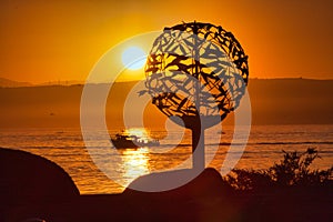 Dramatic orange sky sunset on Monterey Bay with a fishing boat and a sculpture.