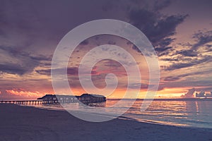 Dramatic beach sunset, luxury water villas with overcast sky. Tropical landscape pattern, soft waves, calm beach resort