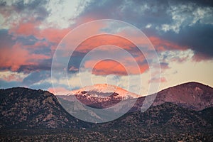 Dramatic, beautiful sunset casts purple and orange colors and hues on clouds and a snow-capped peak near Santa Fe, New Mexico