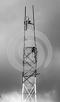 Dramatic black and white image of men working on a communication tower .