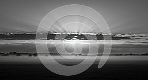 Dramatic black and white landscape showing sunrise clouds and rays