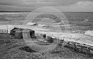 Dramatic black and white seascape with a raging White sea and a fishing hut on the shore. Kandalaksha bay. Umba. Russia