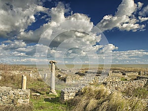 Dramatic blue sky with white clouds over the ruins of an ancient greek column at Histria, on the shores of Black Sea. Histria is