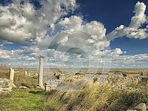 Dramatic blue sky with white clouds over the ruins of an ancient greek column at Histria, on the shores of Black Sea. Histria is