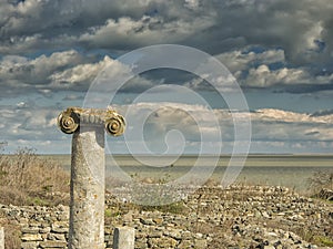 Dramatic blue sky with white clouds over the ruins of an ancient greek column at Histria, on the shores of Black Sea. Histria is