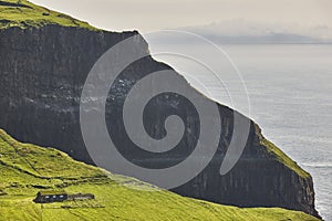 Dramatic cliffs with traditional turf house in Mykines. Faroe