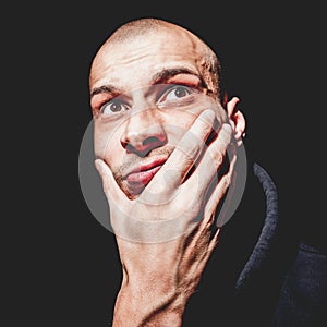 Dramatic close up portrait of young bald man with hand on his face looking up not isolated on black background