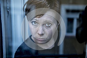 Dramatic close up portrait of young beautiful woman thinking and feeling sad suffering depression at home window looking depresse