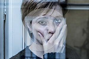 Dramatic close up portrait of young beautiful woman thinking and feeling sad suffering depression at home window looking depresse