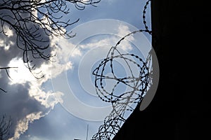 Dramatic clouds behind barbed wire fence on prison wall