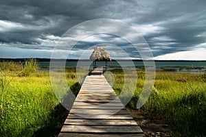 Dramatic clouds behind hut on a dock along the lake shore with dark blue cloudscape, El Remate, Peten, Guatemala