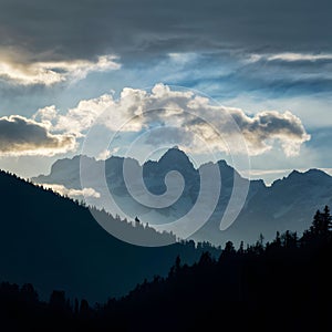 Dramatic clouds frame mountain peaks and towering trees in silhouette