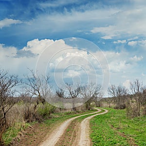 Dramatic clouds over winding road in spring meadow