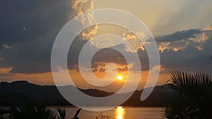 Dramatic clouds during sunset with clouds light rays over the mountains and river with reflections, Thailand