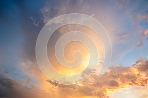 Dramatic cloudscape with puffy clouds lit by orange setting sun and blue sky