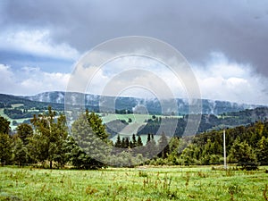 Dramatic cloudy misty mountain ladscape, meadow and forest