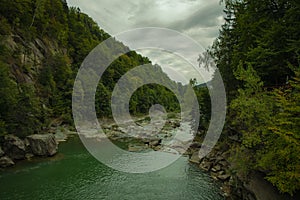 Dramatic cloudy mountain forest landscape highland river stream canyon between rocky edges with green foliage pine trees and gray