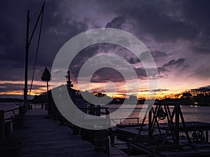Dramatic cloudy nightscape with silhouette of boat house and dock at an empty marina during twilight hours