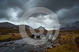 Dramatic cloudy sky with river and old bridge over the River Sligachan on the Isle of Skye Scotland with the Cuillin mountain