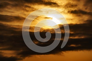 Dramatic cloudy sky at sunset as a background, golden color, sun and dark silhouettes of clouds