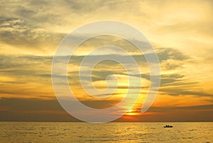 Dramatic colorful sea sunset with sun setting on water lonely boat on horison