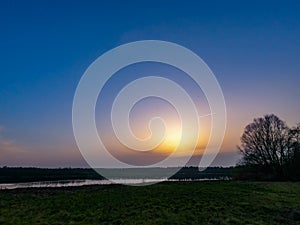 Dramatic and colorful Sunrise or sunset on a field covered with young green grass and yellow flowering dandelions in