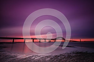 Dramatic deep purple clouds pre dawn over a bridge stretching across a body of water. Fire Island Inlet Bridge - Long Island NY