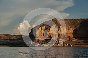 Dramatic desert rock formation rising above a lake with cloud and sky background