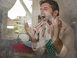 Dramatic grunge portrait of  house husband or single man in kitchen apron doing domestic chores washing dishes or cooking in