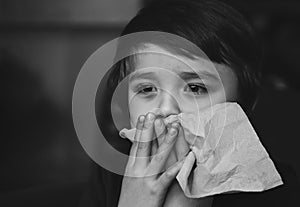 Dramatic image of Sick kid blowing nose into tissue, Unhealthy child suffering from running nose or sneezing and covering his nose