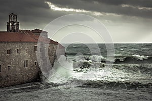 Dramatic landscape with ancient castle on sea shore during storm with big stormy waves and dramatic sky with rain in fall season o