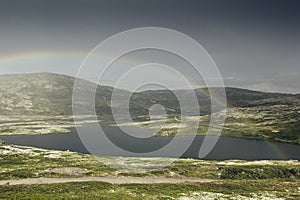 Dramatic landscape with beautiful rainbow over arctic meadows, mountain and lake.