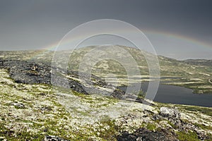 Dramatic landscape with beautiful rainbow over arctic meadows, mountain and lake.