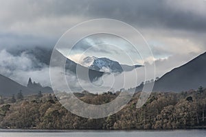 Dramatic landscape image looking across Derwentwater in Lake District towards Catbells snowcapped mountain with thick fog rolling