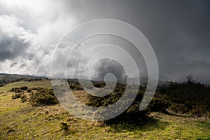 Dramatic landscape of storm clouds, fog, and grassy meadow and hills