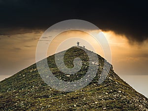 Dramatic landscape with three hikers reaching the top of the mountain. Pyramid shaped mountain peak in Bucegi Mountains