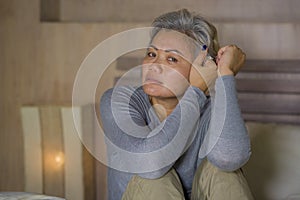 Dramatic lifestyle home portrait of attractive sad and depressed middle aged woman with grey hair on bed feeling upset suffering