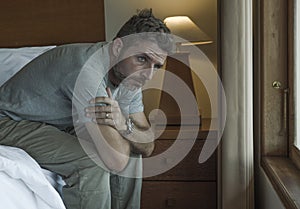 Dramatic lifestyle portrait of handsome guy sitting on bed feeling sad thinking and suffering depression and anxiety problem