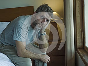 Dramatic lifestyle portrait of handsome guy sitting on bed feeling sad thinking and suffering depression and anxiety problem