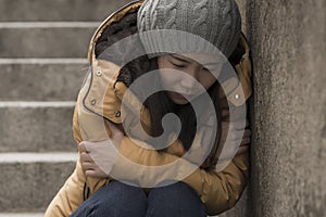 Dramatic lifestyle portrait of young attractive sad and depressed Chinese woman in winter hat sitting outdoors on street corner