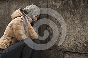 Dramatic lifestyle portrait of young attractive sad and depressed Japanese woman in winter hat sitting outdoors on street corner