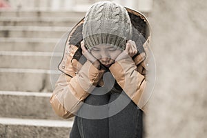 Dramatic lifestyle portrait of young attractive sad and depressed Korean woman in winter hat sitting outdoors on street corner